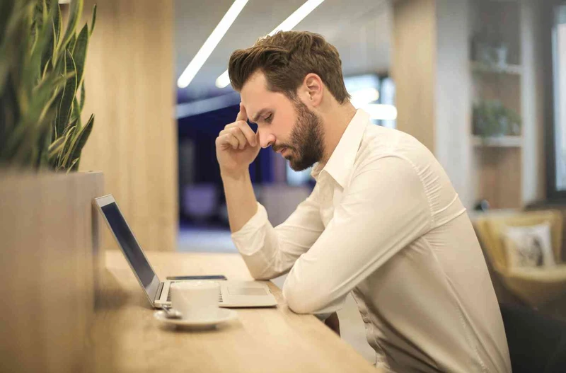 Mann sitzt mit Kopfschmerzen vor dem Laptop